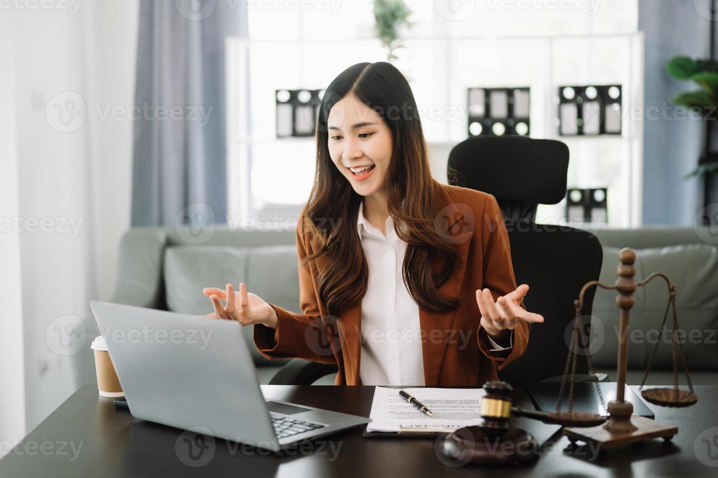 asiático hembra abogado chateando en línea con cliente en computadora portátil, teléfono inteligente que se discute detalles de demanda judicial. en moderno oficina foto