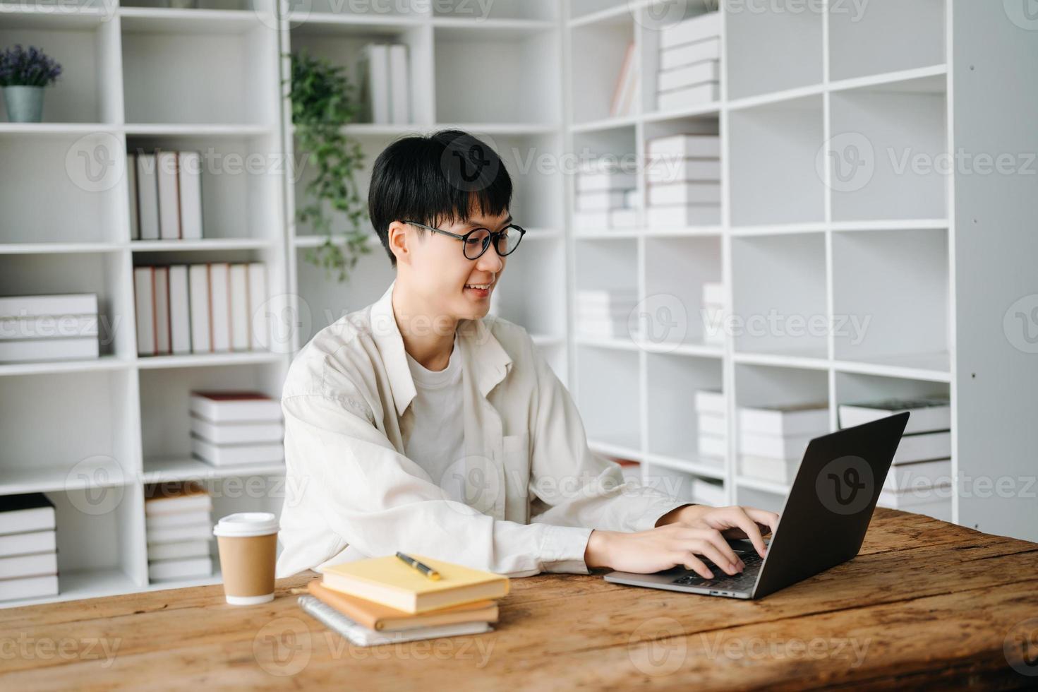 hermoso y talentoso joven asiático hombre estudiante trabajando en su proyecto asignación, utilizando ordenador portátil y tableta a buscar un en línea informaciones foto