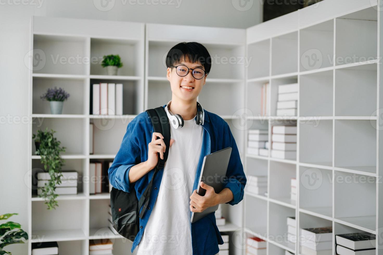 masculino estudiante tomando notas desde un libro a biblioteca, joven asiático sentado a escritorio haciendo asignaciones en Universidad biblioteca foto