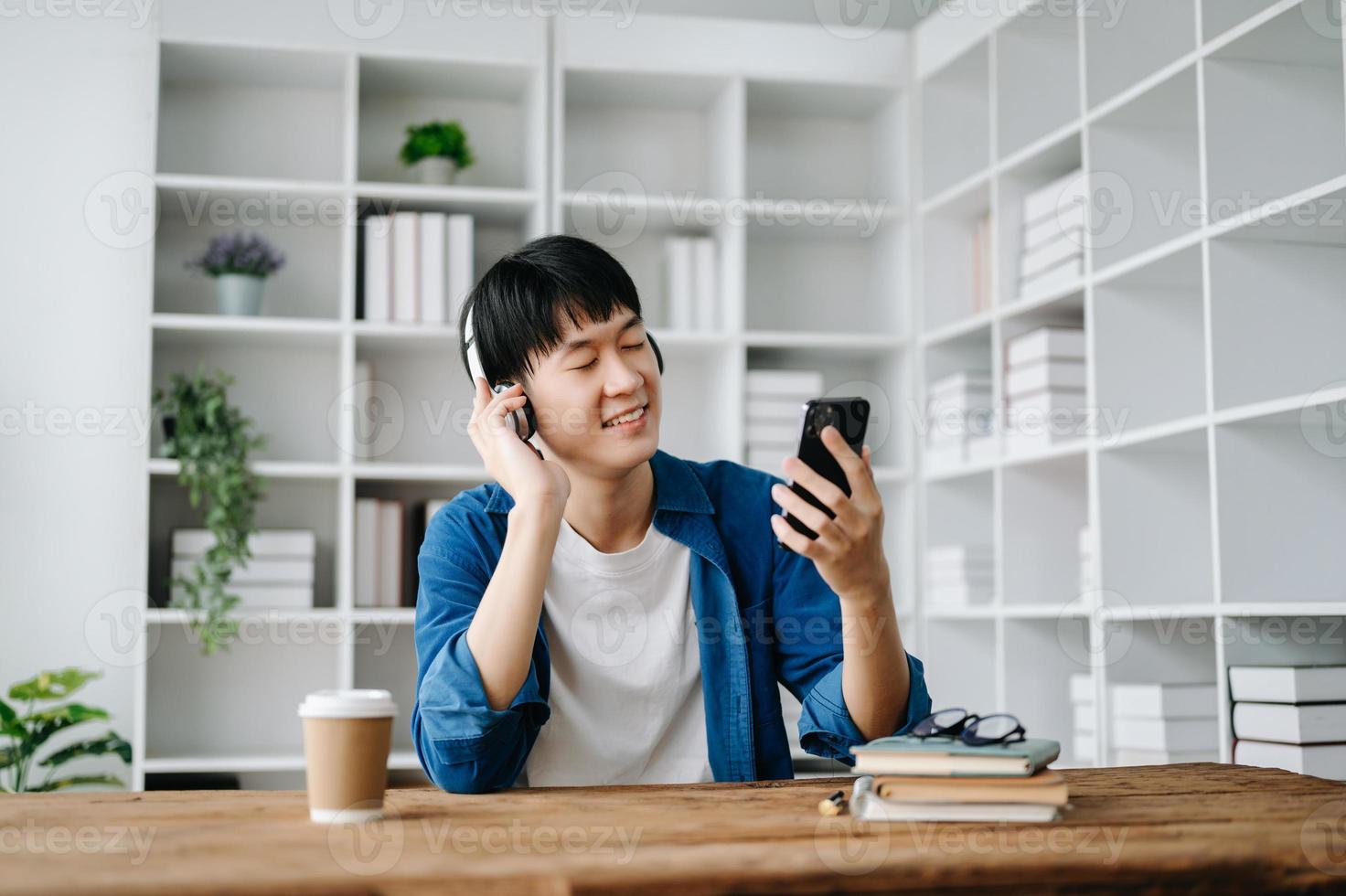 sonriente masculino relajante a hogar, ella es jugando música utilizando teléfono inteligente tableta, computadora portátil, y vistiendo blanco auriculares. en mesa foto