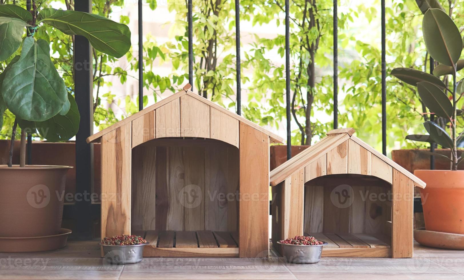 two empty wooden dog's houses with dog food bowls  in balcony decorated with houseplant in plant pots. photo