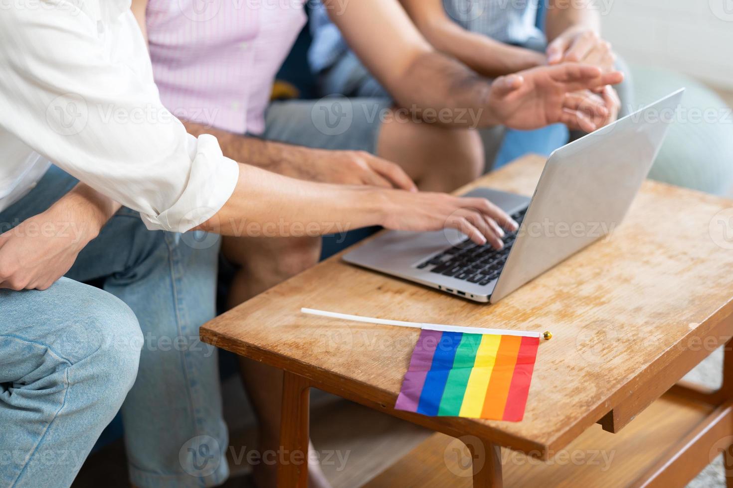 triple joven hombre sentado en el vivo habitación mientras utilizando ordenador portátil a vídeo llamada con arco iris bandera en escritorio. lgbtq personas estilo de vida y amor emoción. lgbt social red. selectivo atención foto