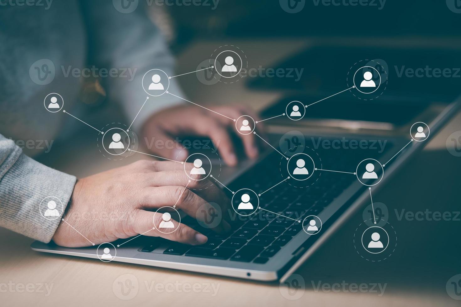 Hand using laptop to play social media, a mobile phone with a notification people icon,Social Distancing ,Working From Home concept,international consulting company. Social networking hologram icons. photo