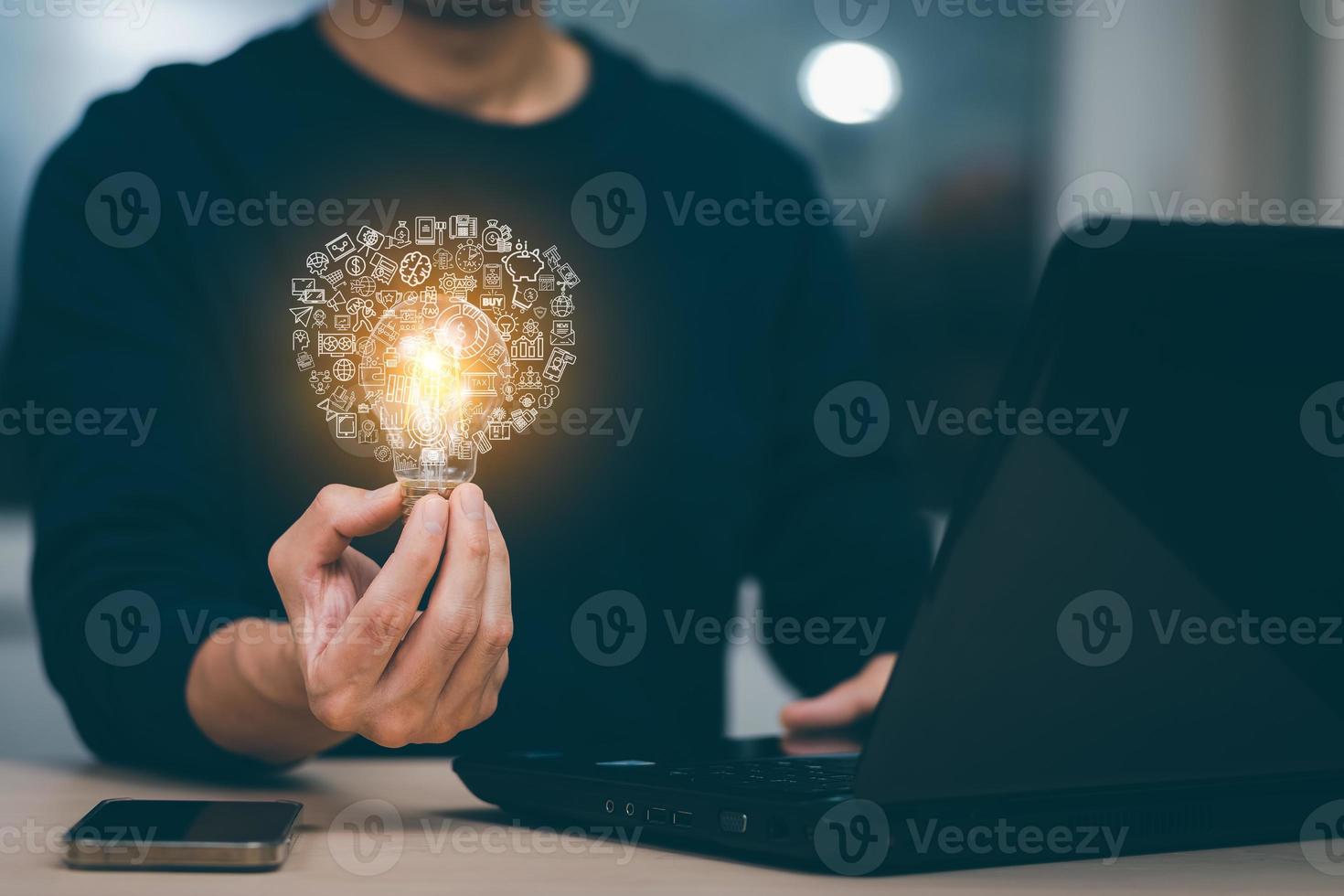 Businessman hand holding light bulb with icons and working on the desk, Creativity and innovation are keys to success.Concept of new idea and innovation with energy and power , working at home, photo