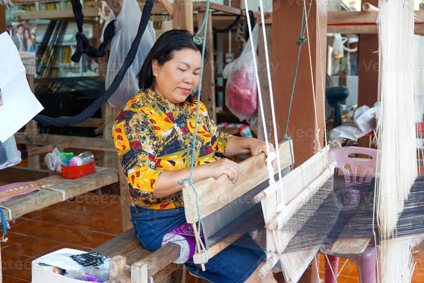 Asian women tourists try weaving with a hand loom in the concept of OTOP, community products, hand weaving fabrics, community shops, community weaving centers, community tourist attractions. photo