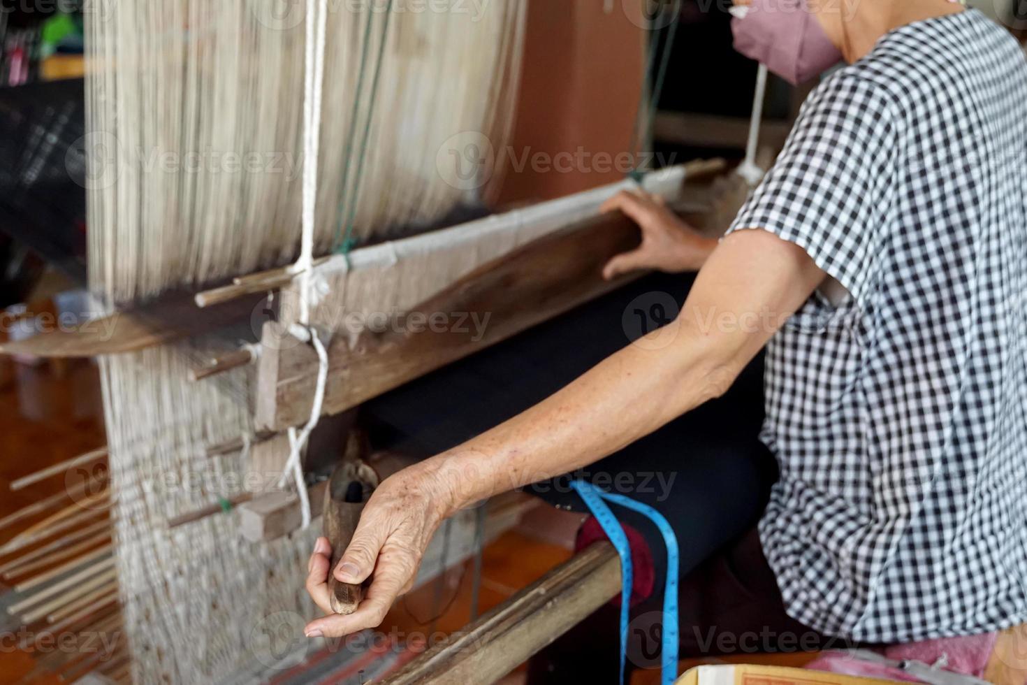 Asian female weavers weaving traditional patterns with hand weaving machines.in the concept of OTOP, community products, hand weaving fabrics, community shops, community weaving centers. photo