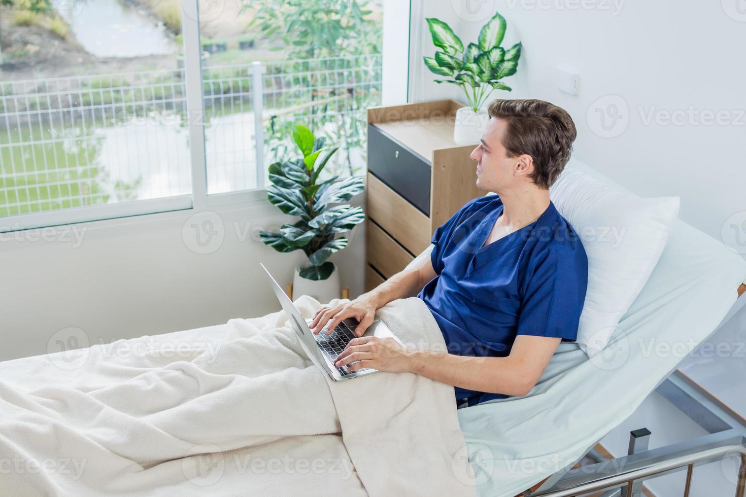 Caucasian patient using laptop in hospital room. man sick patient lying in a hospital bed photo