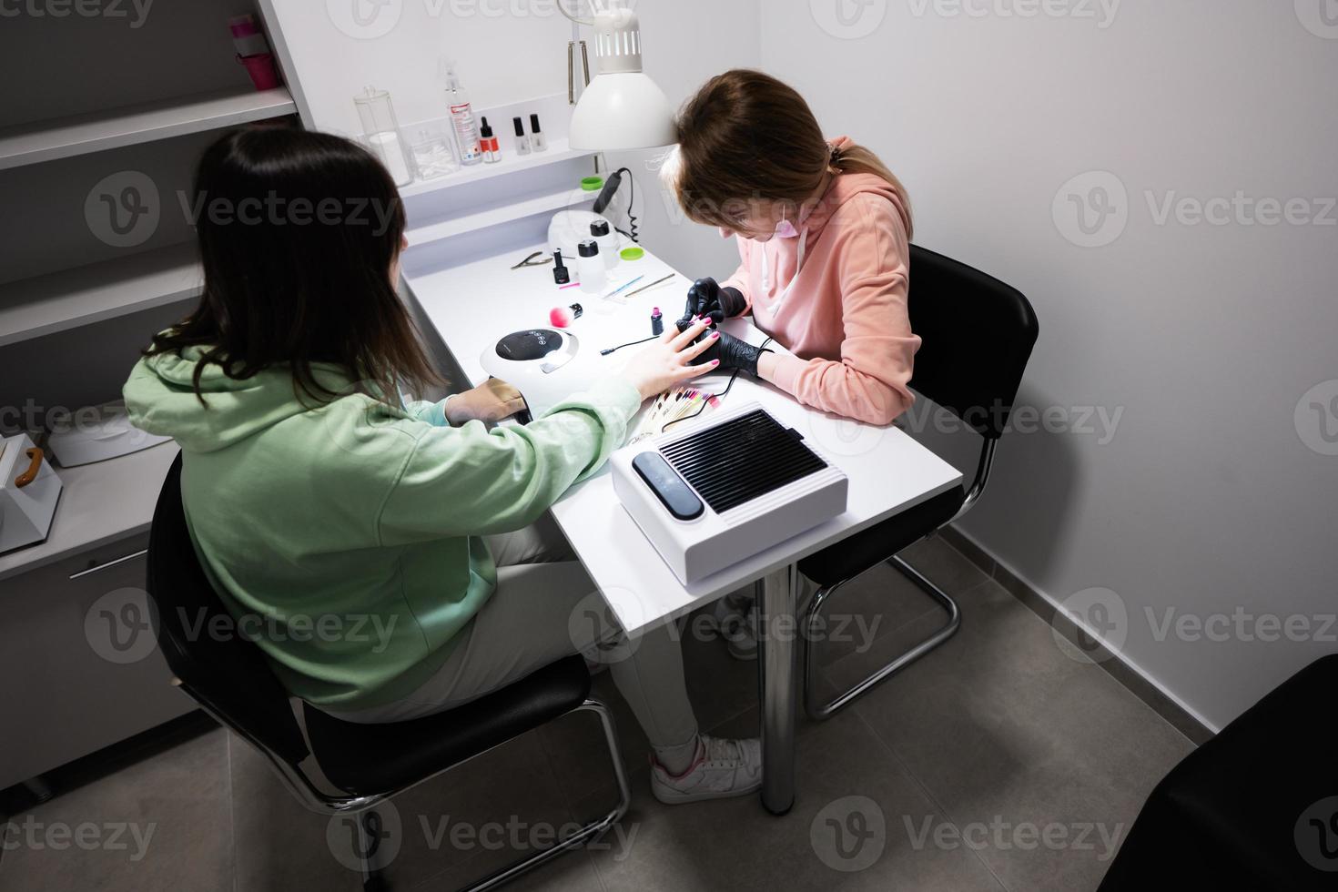 Manicure master working with female client in beauty salon. Manicurist makes woman nail. photo