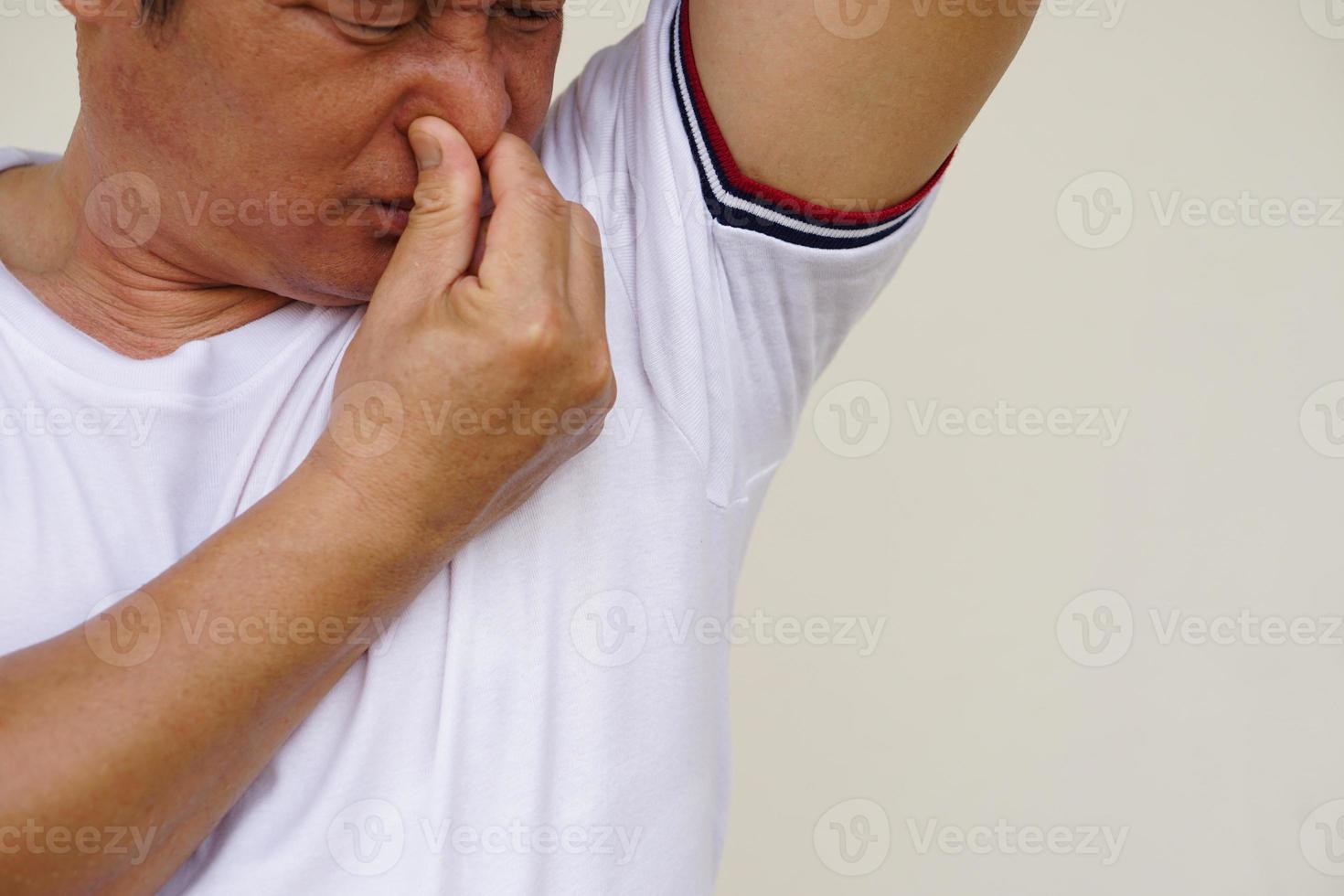 Closeup Asian man checks his body odor during he feels hot, raises right arm up, smells his armpit, underarm. Concept  health problem. Unpleasant body odor , smell nasty reaction. Negative emotion. photo