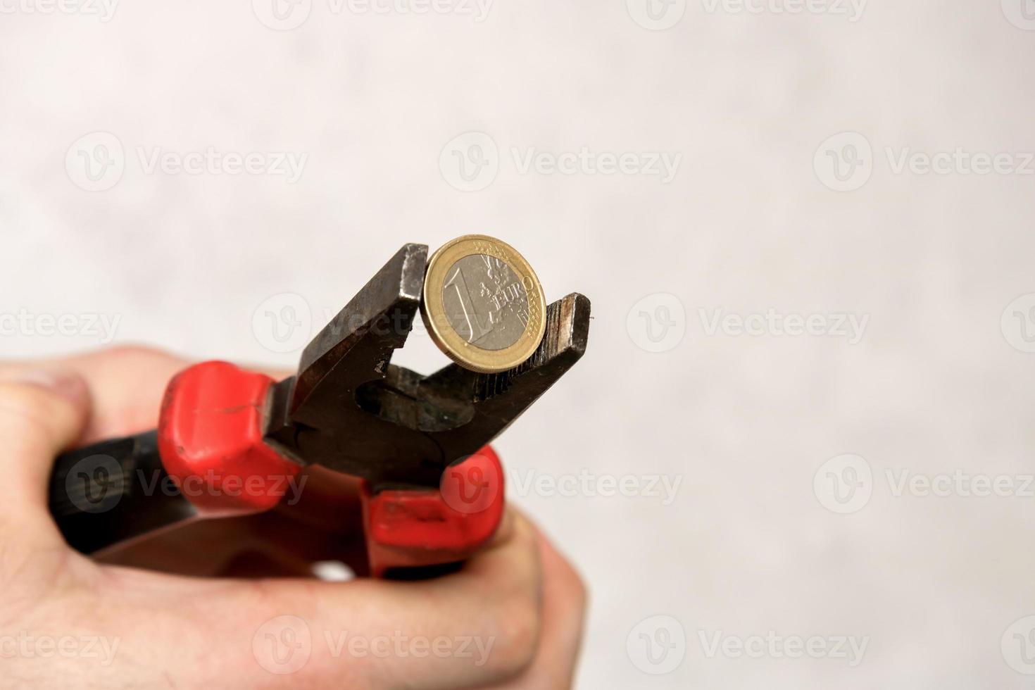 man's hand holds 1 euro in a vice, financial crisis photo