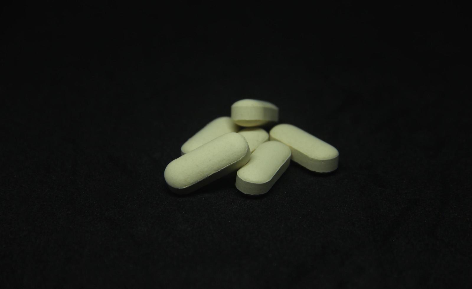 Yellow vegetable tablet medicine supplement for illnes and daily healthcare. A bunch of pills photography isolated on dark black background. photo