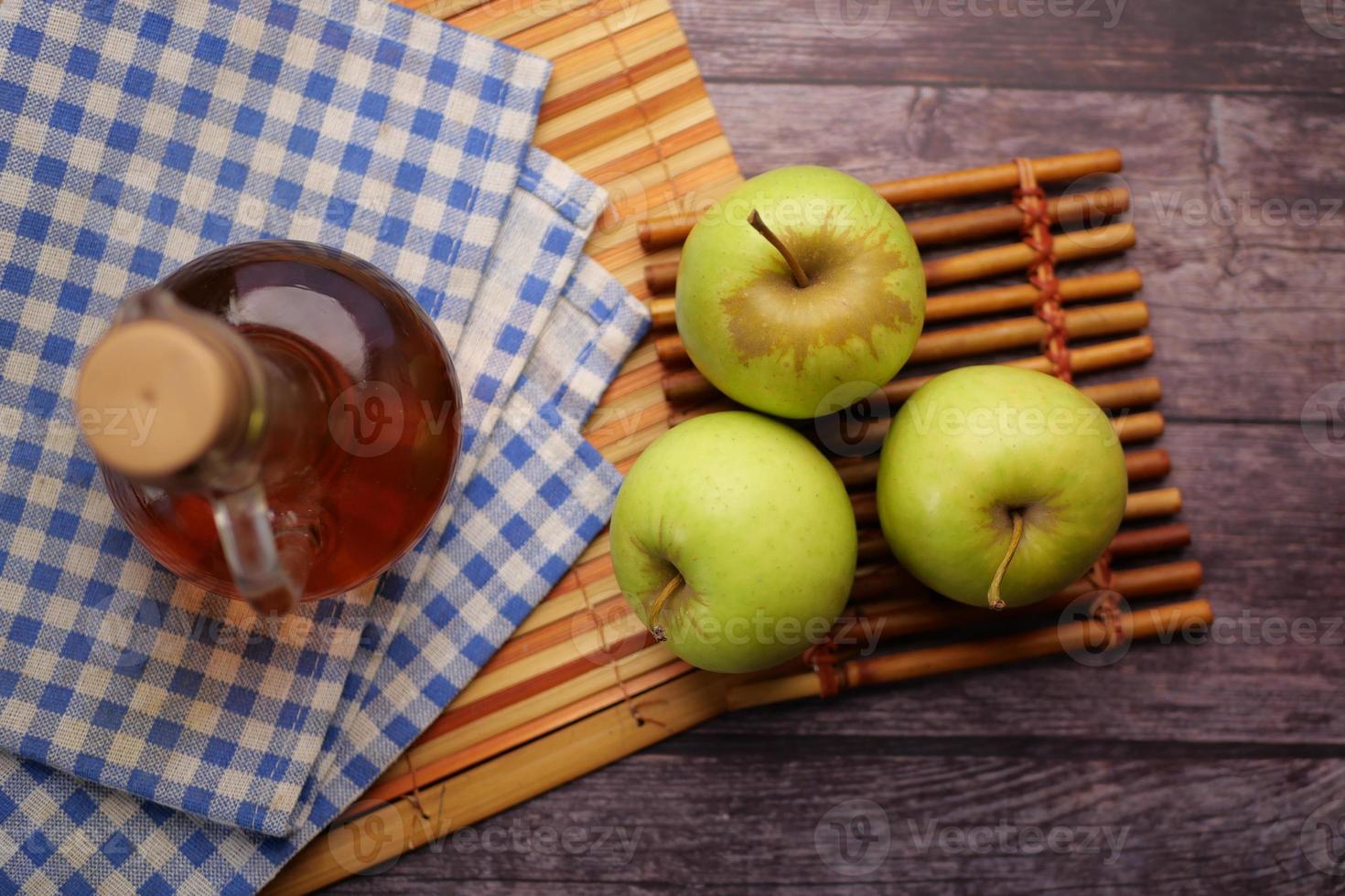 Vinagre de manzana en botella de vidrio con manzana verde fresca en la mesa foto