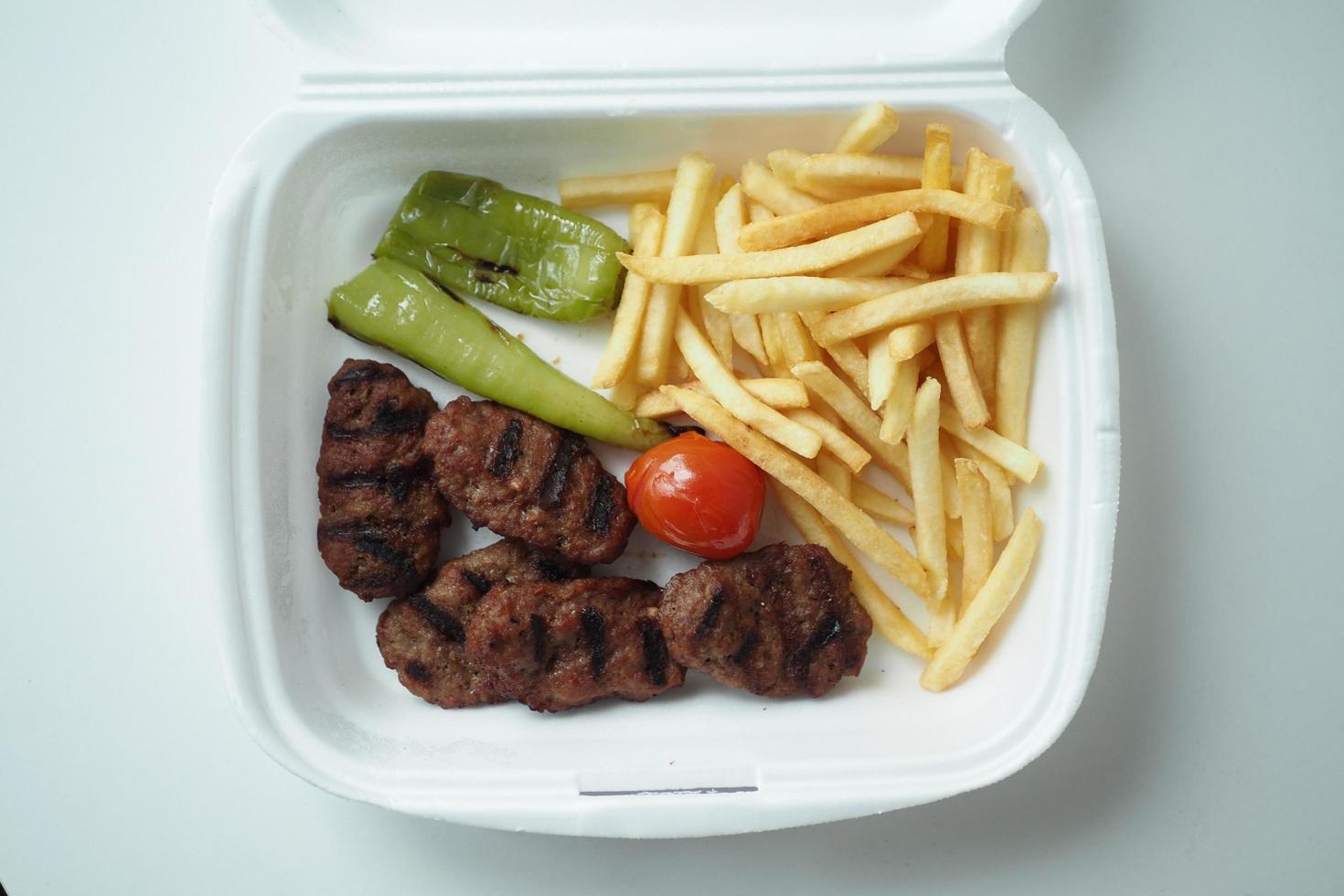 Kabab meat with potato fries in a take away packet on table photo