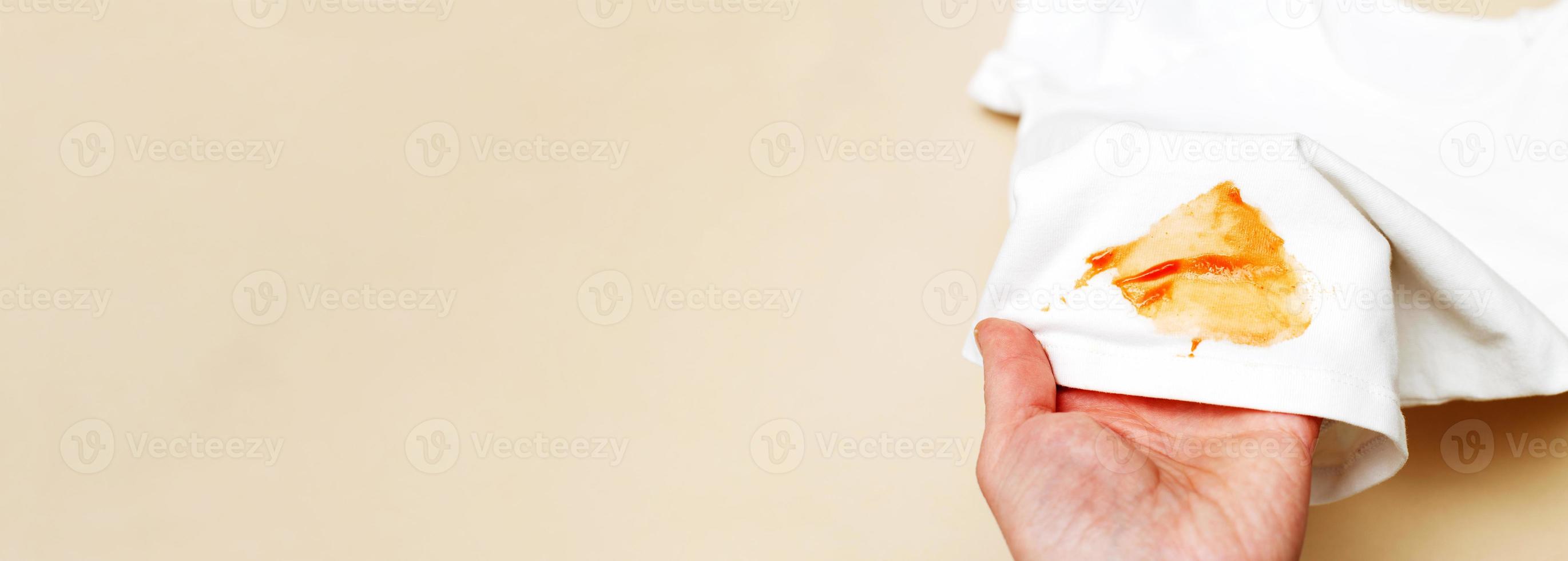 womans hand hold white shirt clothes with ketchup stain on a beige background. banner photo