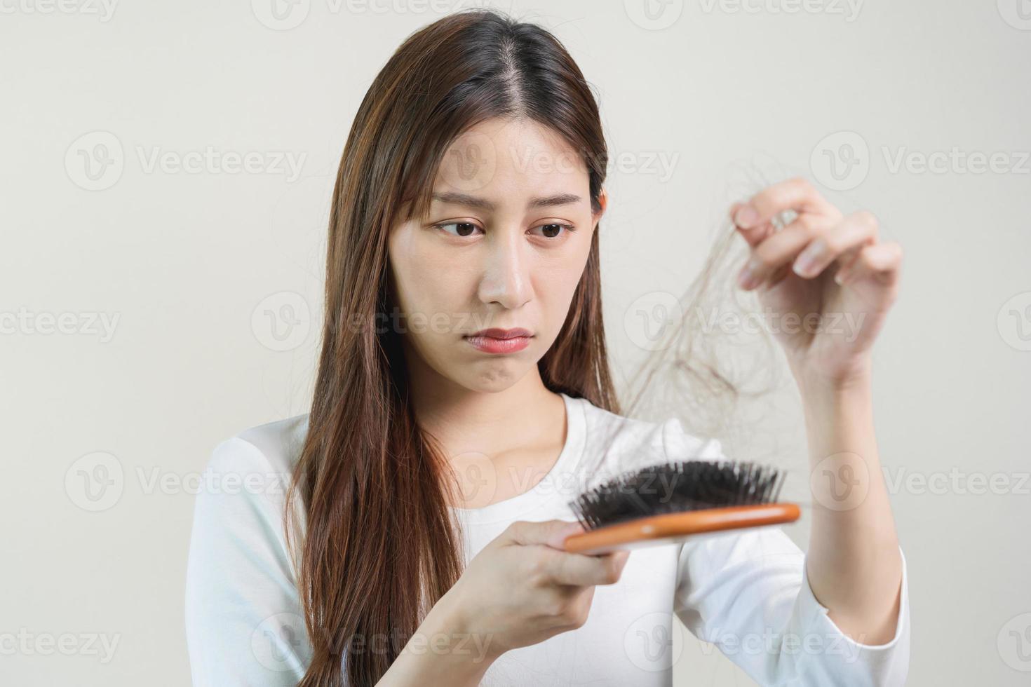 grave, preocupado asiático joven mujer, niña participación cepillar, espectáculo su peine, cepillo para el pelo con largo pérdida pelo problema después cepillado, pelo otoño fuera en su mano en vivo habitación. salud cuidado, belleza tratamiento. foto