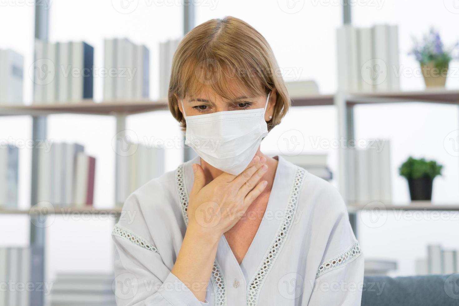 enfermo, herir o dolor, debilidad caucásico maduro adulto, mayor mujer vistiendo máscara con dolorido garganta, dolor de cabeza tener fiebre, gripe o debilidad, sentado en sofá cama a hogar. salud cuidado persona en virus estacional foto