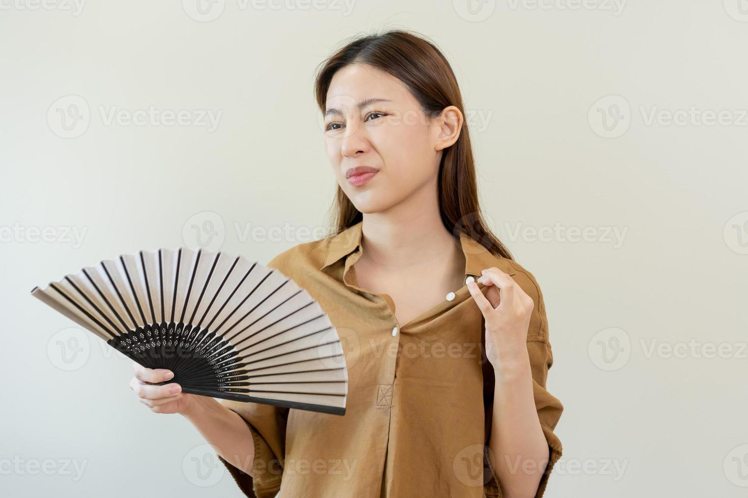 Suffering summer heat stroke, hot weather, tired asian young woman, girl sweaty and thirsty, refreshing with hand in blowing, wave fan to ventilation when temperature high at home, house on background photo