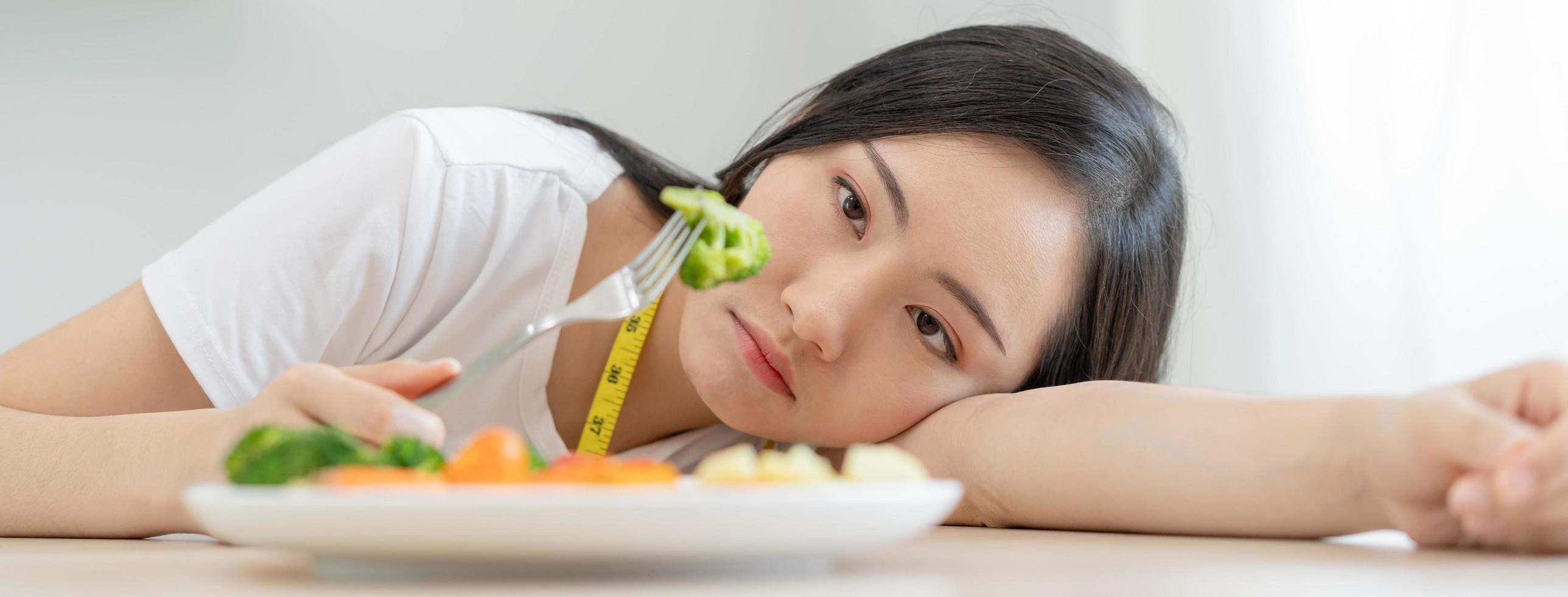 Diet in bored face, unhappy beautiful asian young woman, girl on dieting, holding fork in salad plate, dislike or tired with eat fresh vegetables. Nutrition of clean, healthy food good taste. photo