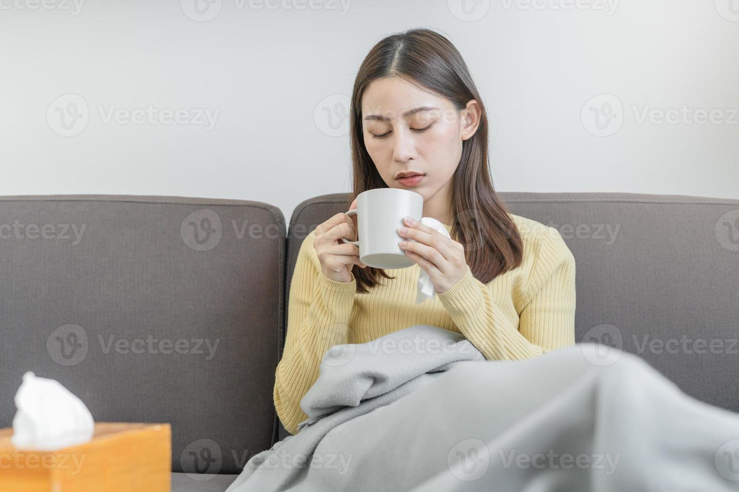 enfermo, herir o dolor asiático joven mujer, niña dolorido garganta con vaso, jarra de calentar agua, dolor de cabeza tener un fiebre, gripe en debilidad, sentado relajado en sofá cama a hogar. salud cuidado persona en virus estacional. foto