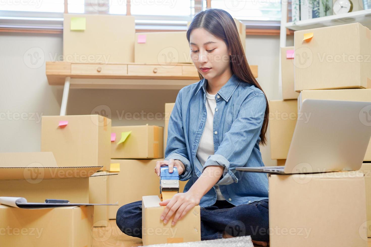 empresaria de pequeñas empresas, joven asiática, propietaria de una niña empacando productos, revisando el paquete para entregarlo al cliente, usando cinta adhesiva para sellar la caja, trabajando en casa. comerciante en línea, comercio electrónico foto