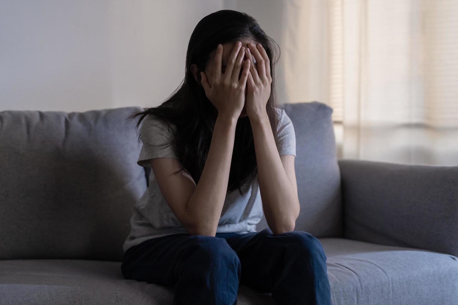 Mental health, depressed sad asian young woman, girl sitting on sofa, couch, expression to face difficulty, failure and exhausted. Thoughtful worried suffering depression feeling lonely, alone at home photo