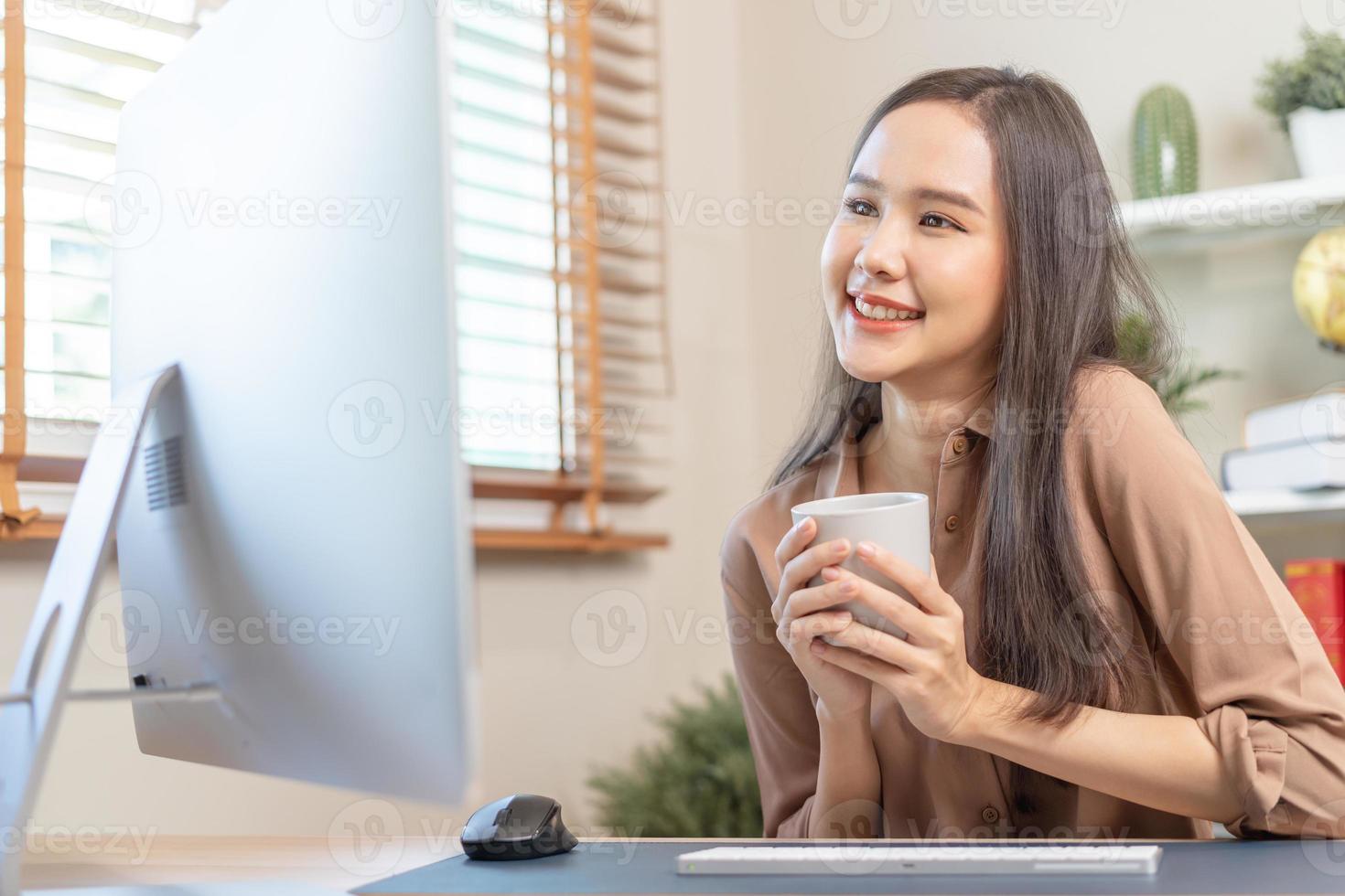 Freshness, beautiful asian young business woman holding cup coffee or drinking, freelancer working on PC compute sitting her house.Technology, social distance of work from home, office in covid-19. photo