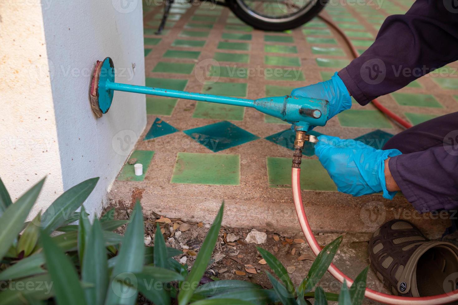 exterminate termite control company employee is using a termite sprayer at customer's house and searching for termite nests to eliminate. exterminate control worker spraying chemical insect repellant photo