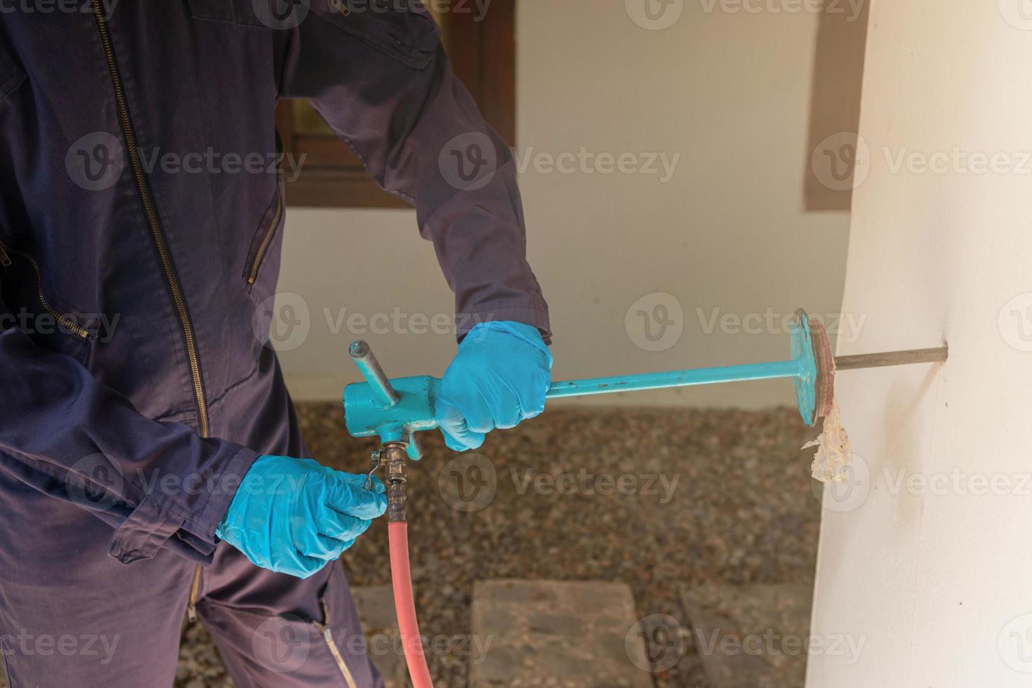 exterminate termite control company employee is using a termite sprayer at customer's house and searching for termite nests to eliminate. exterminate control worker spraying chemical insect repellant photo