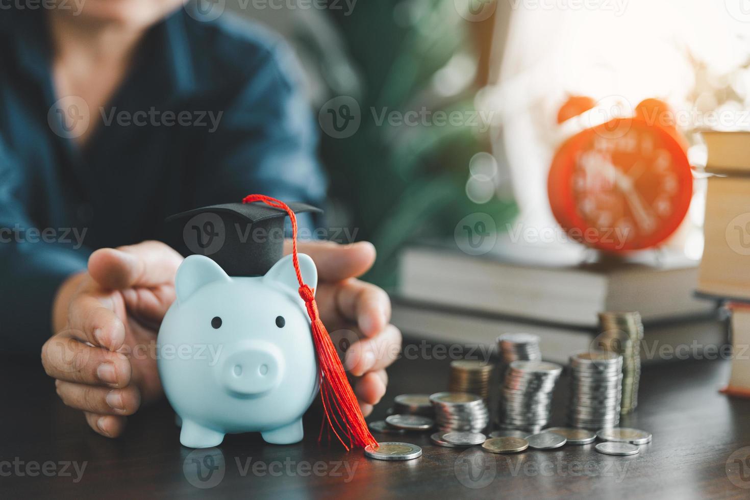 Hands protecting graduation cap on piggy bank with stack coins. Concept of saving money for scholarship to study abroad at university level. Financial planning accounting ideas for future education. photo