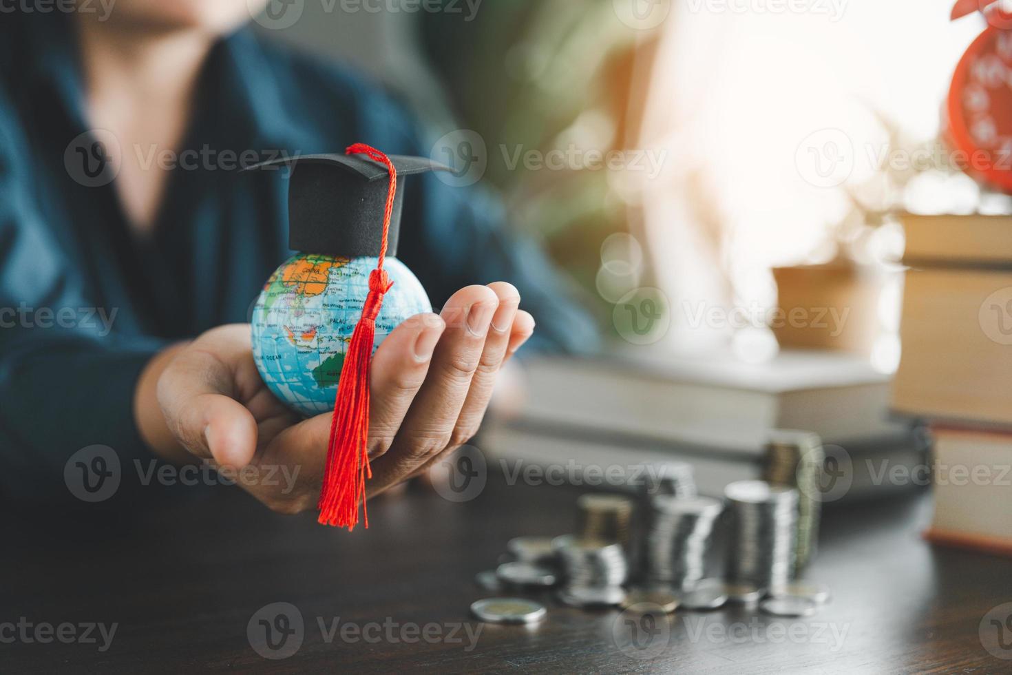 Hand holding graduation cap on globe with stack coin. Concept of saving money for a scholarship to study abroad at a university level. Financial planning accounting ideas for future education. photo