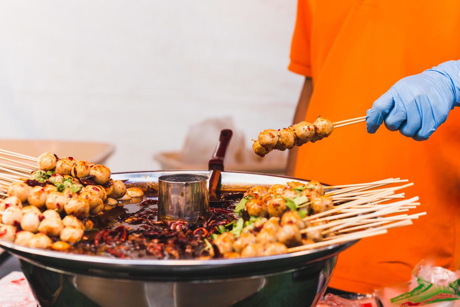 Food vendor hand holding pork meatballs in skewer with sweet chili sauce. photo