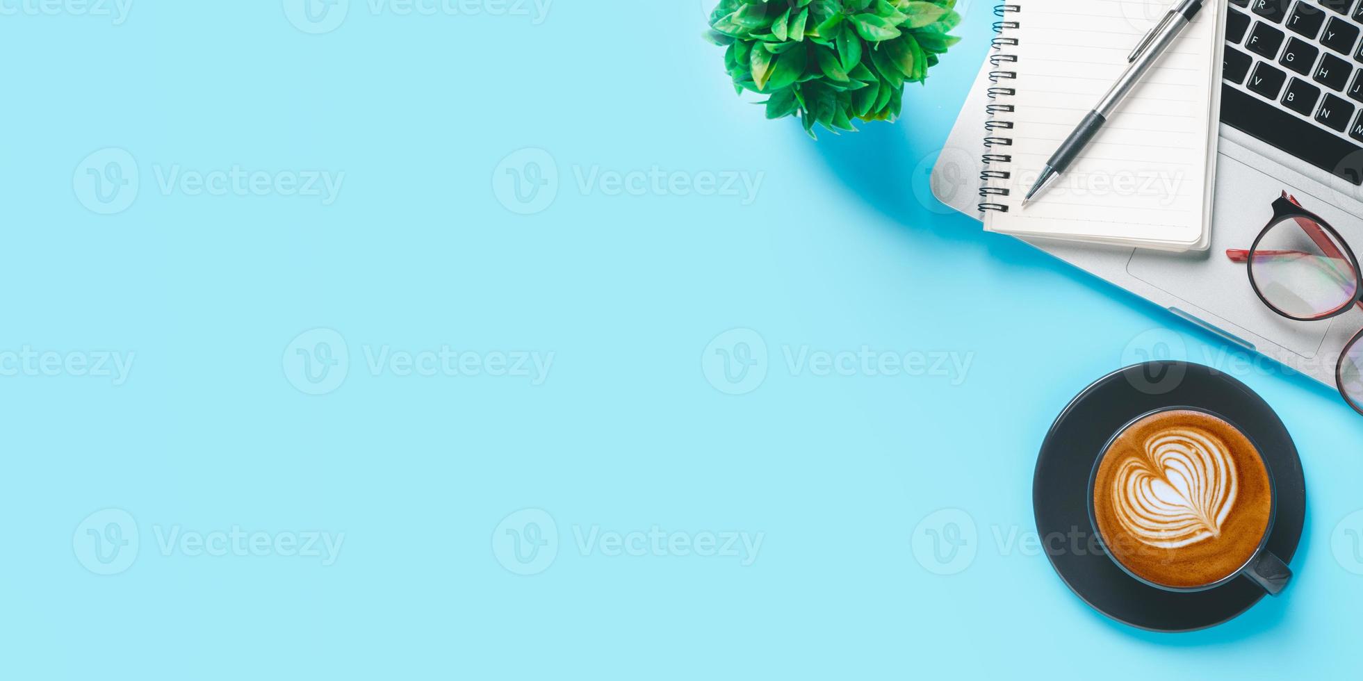 Office desk with computer, Pen, eyeglass, notebook, Cup of coffee on blue background, Top view with copy space, Mock up. photo