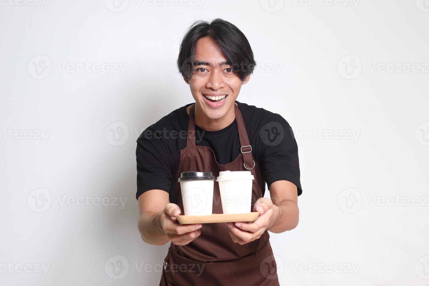 retrato de atractivo asiático barista hombre en marrón delantal participación dos tomar lejos papel café tazas. aislado imagen en blanco antecedentes foto