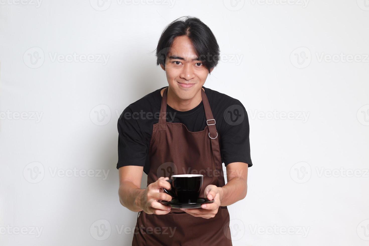 Portrait of attractive Asian barista man in brown apron serving a cup of coffee to the customer. Isolated image on white background photo