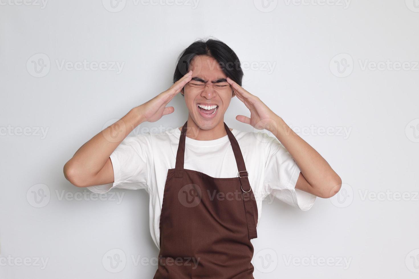 Portrait of attractive Asian barista man in brown apron holding hand on forehead, forgets something, and regrets himself. Isolated image on white background photo