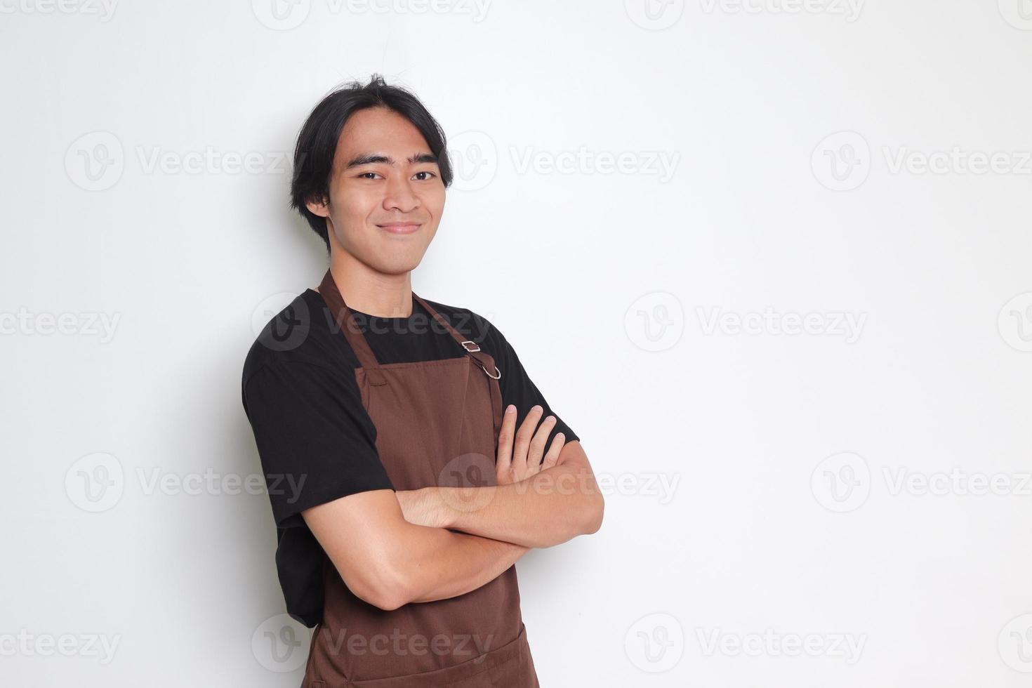 Portrait of attractive Asian barista man in brown apron keeping arms crossed and looking at camera. Advertising concept. Isolated image on white background photo