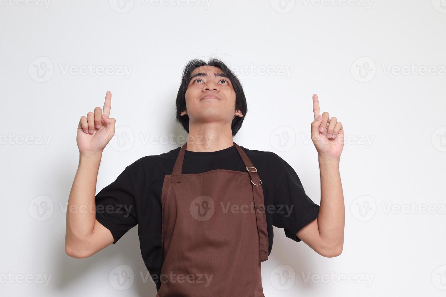 Portrait of attractive Asian barista man in brown apron showing product, pointing at something with hands. Advertising concept. Isolated image on white background photo