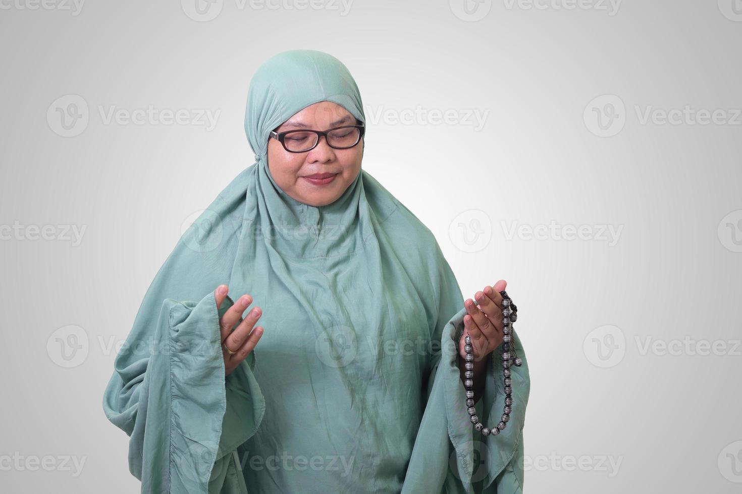 Portrait of Asian woman wearing prayer gown or mukena while praying with hands raised. Isolated image on white background photo