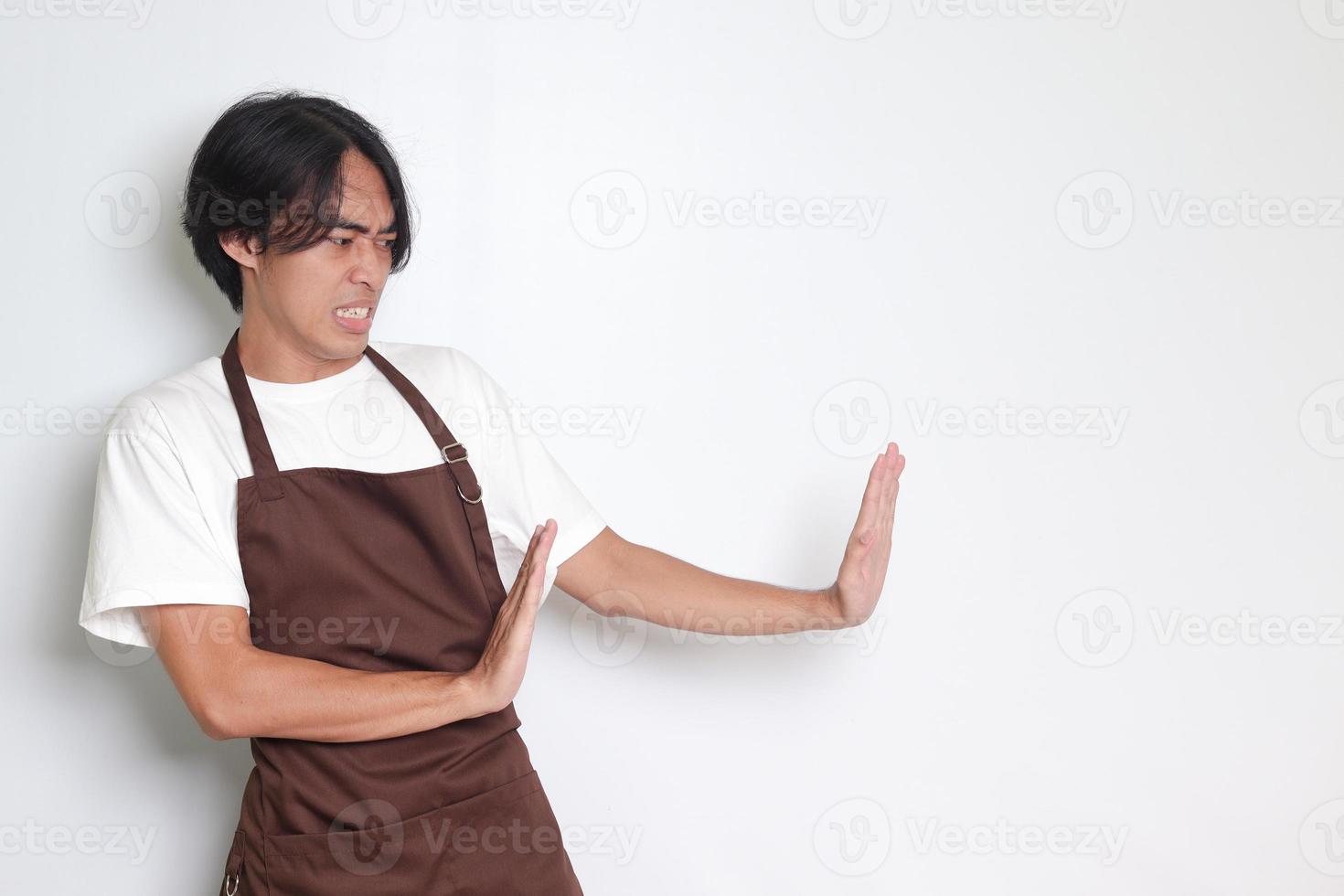 retrato de atractivo asiático barista hombre en marrón delantal formando un mano gesto a evitar algo. aislado imagen en blanco antecedentes foto