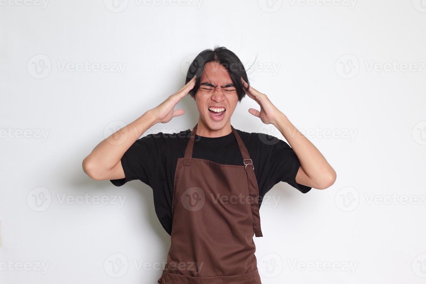 Portrait of attractive Asian barista man in brown apron holding hand on forehead, forgets something, and regrets himself. Isolated image on white background photo
