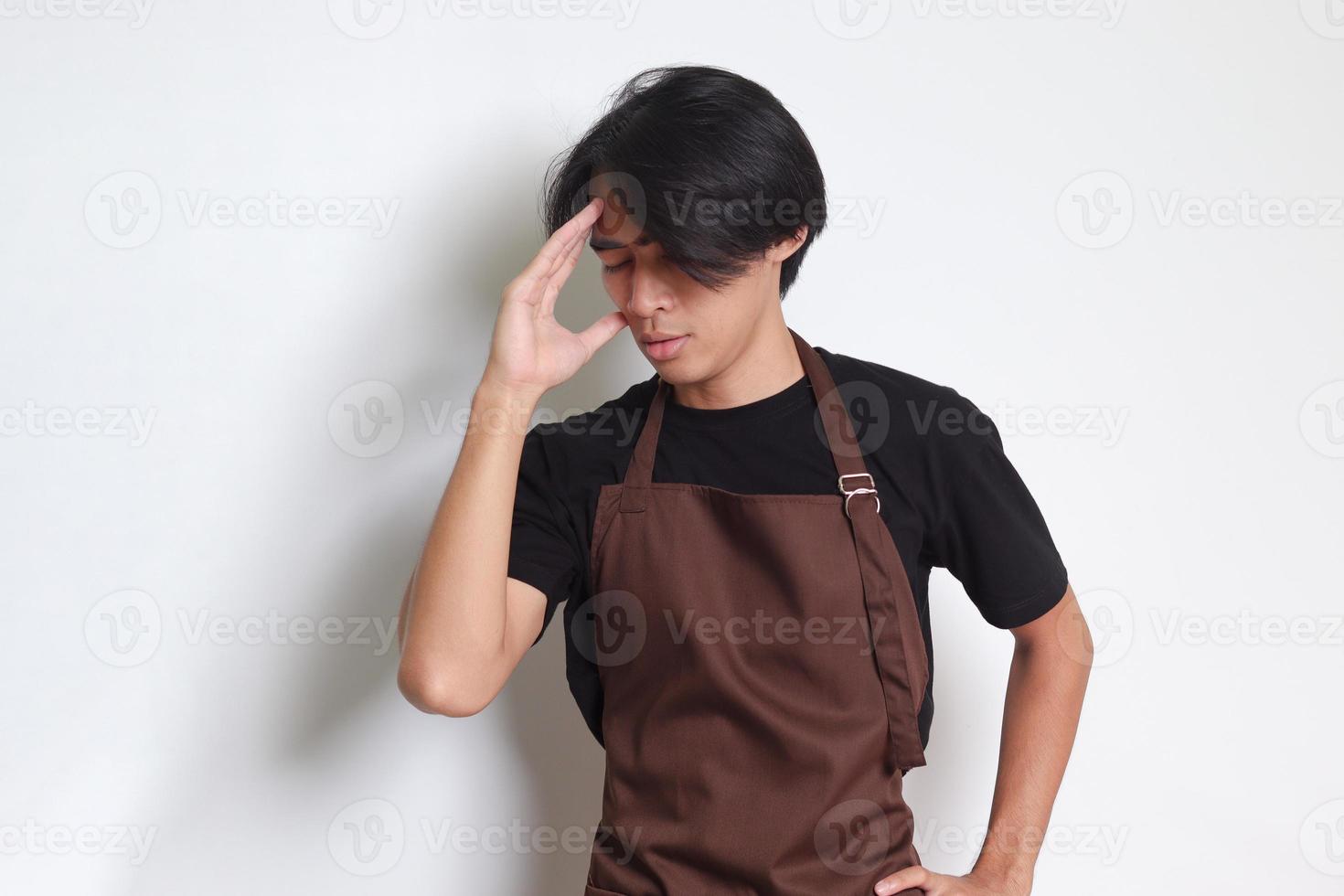 Portrait of attractive Asian barista man in brown apron holding hand on forehead, forgets something, and regrets himself. Isolated image on white background photo