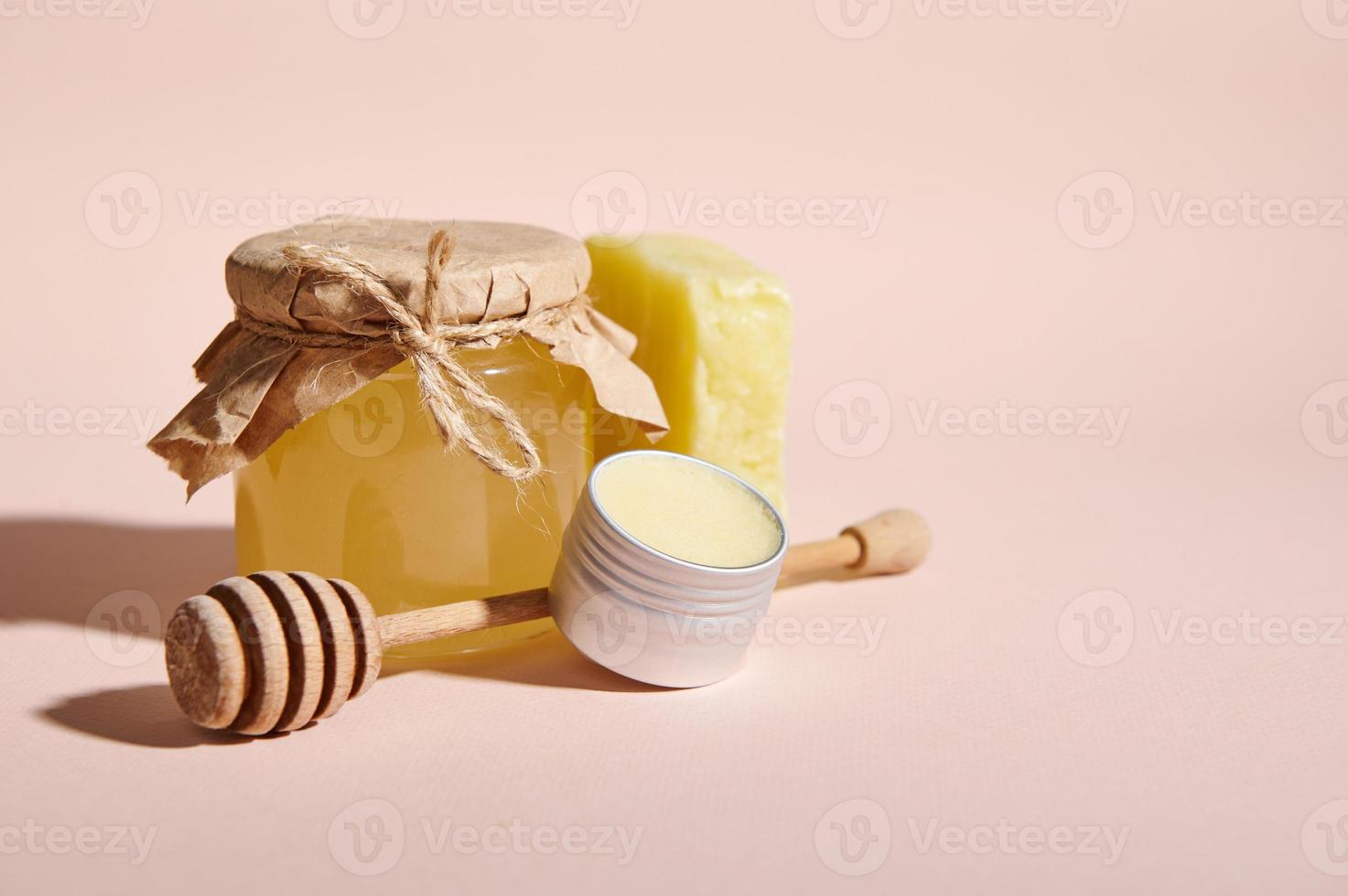 Still life. Organic honey and wooden stick on pink backdrop, next to natural handmade cold-pressed soap and can of wax photo