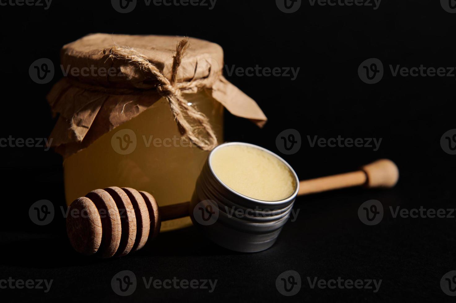 todavía vida con orgánico miel en vaso frasco, lata con cera y de madera miel cuchara, aislado en negro antecedentes foto