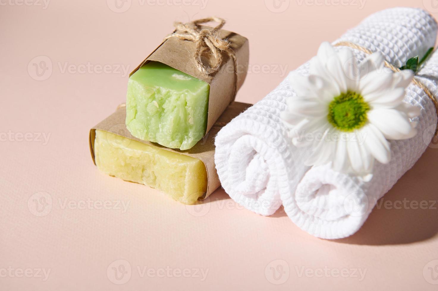 Still life. Towels and organic soap bars and dry solid shampoos, wrapped in eco paper, isolated on pink backdrop. photo