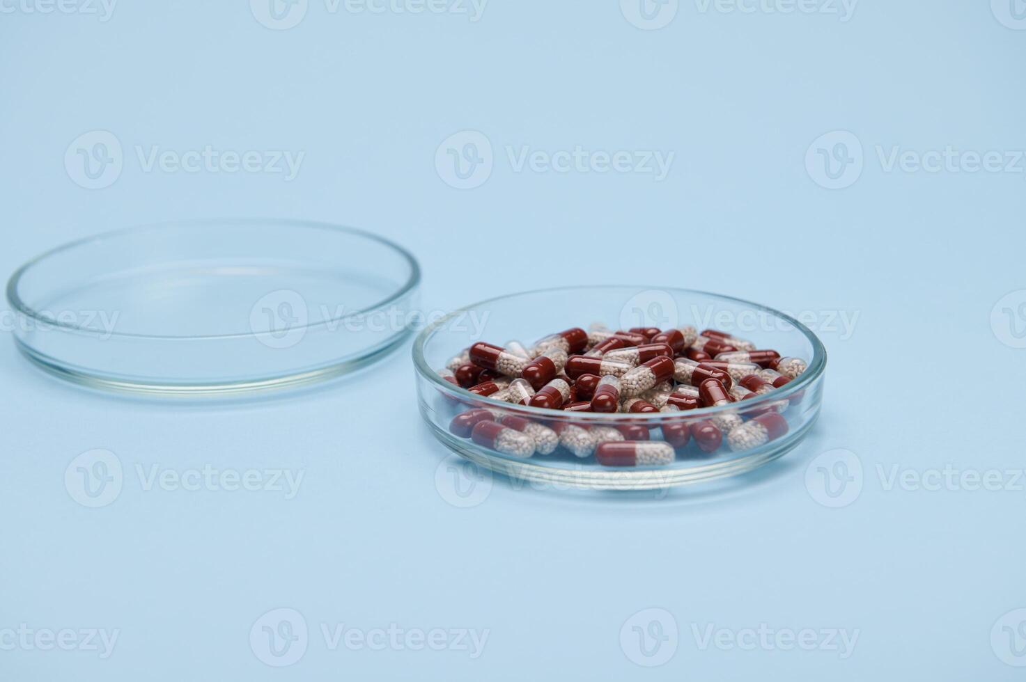 A petri dish with medical pills and gelatin capsules on isolated blue
