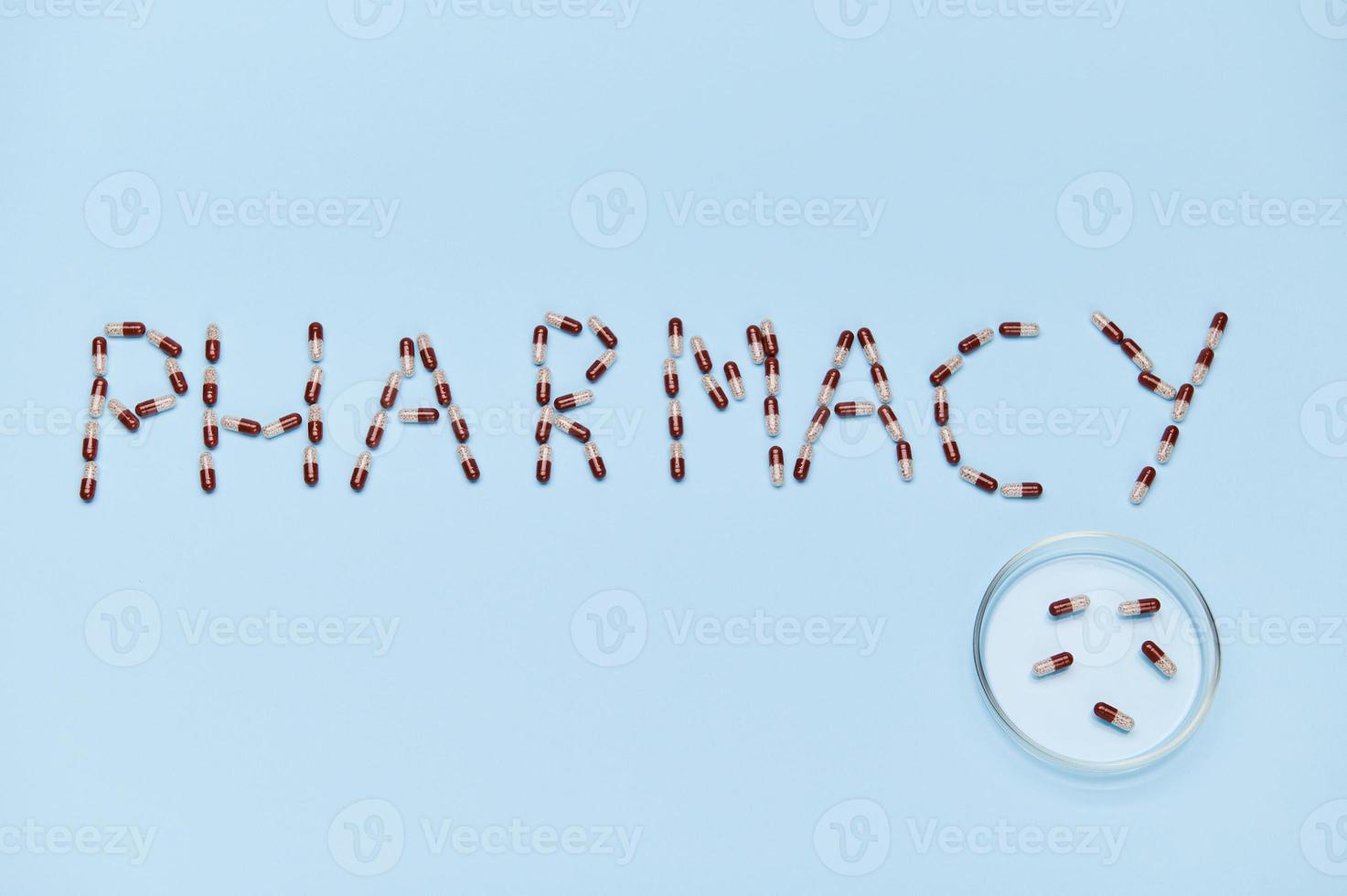 The word PHARMACY laid out on blue background next to Petri dish with medical capsules. Copy space. World Pharmacist Day photo