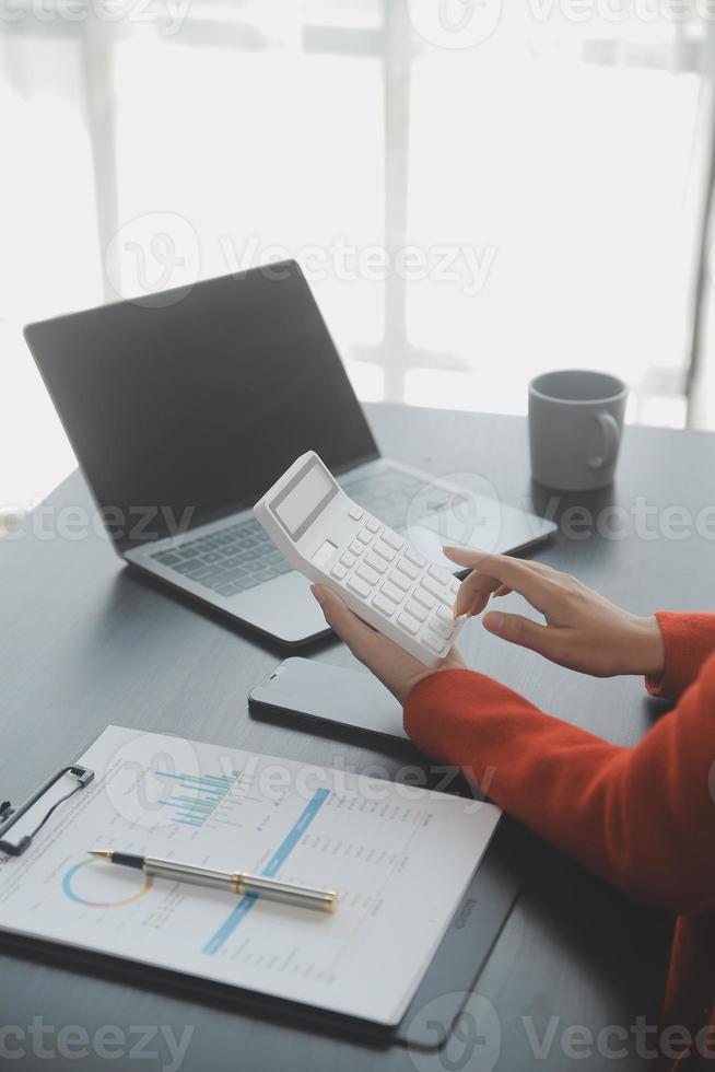 Asian Businesswoman Using laptop computer and working at office with calculator document on desk, doing planning analyzing the financial report, business plan investment, finance analysis concept. photo