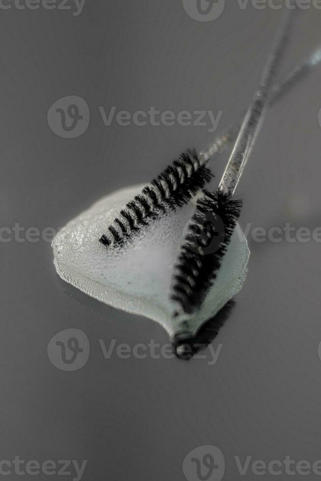 Two black cosmetic brushes for eyebrows and eyelashes lie on a wet table photo