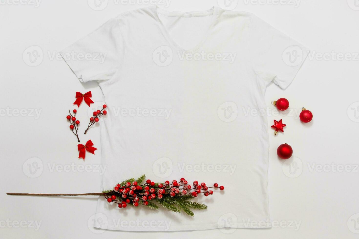 Close up white blank template t shirt with copy space and Christmas Holiday concept. Top view mockup t-shirt and red holidays decorations on white background. Happy New Year accessories. Xmas outfit photo