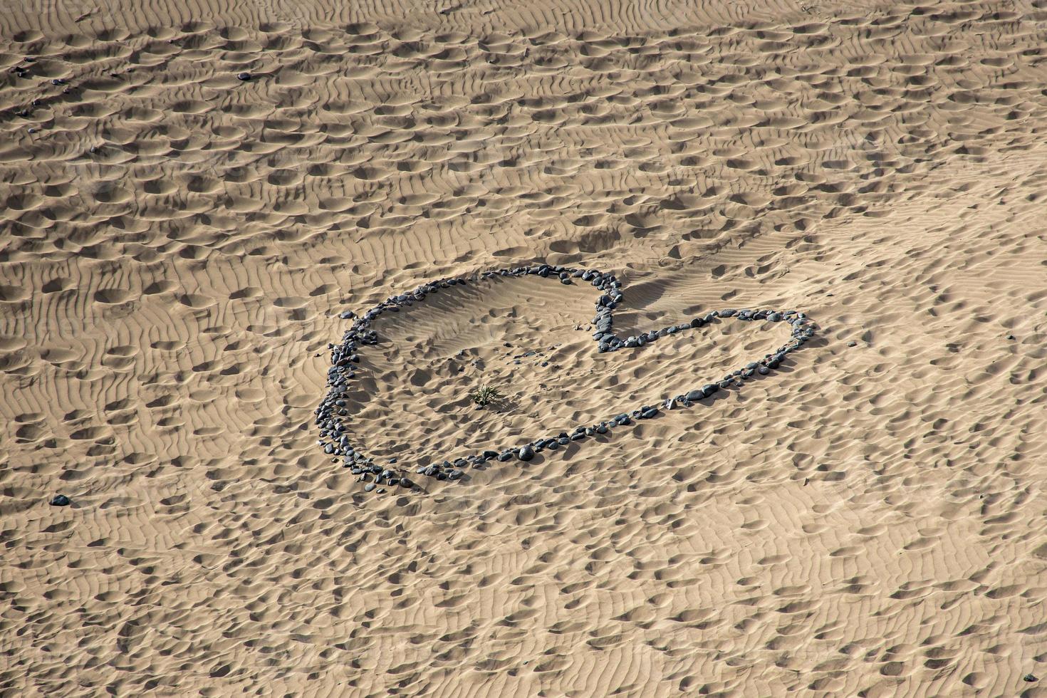 heart symbol of love arranged from gray stone on golden sand on a golden dune photo